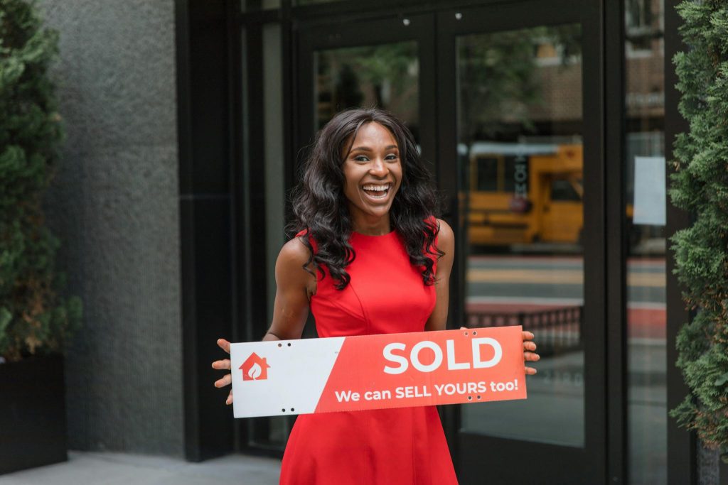 Crafting the Perfect Blog Structure: A Guide for Effective Blogging Smiling woman in red dress holding sold sign outside an office building.
